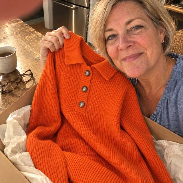 The orange Elyon dress held up out of its box, showing the collar and three buttons